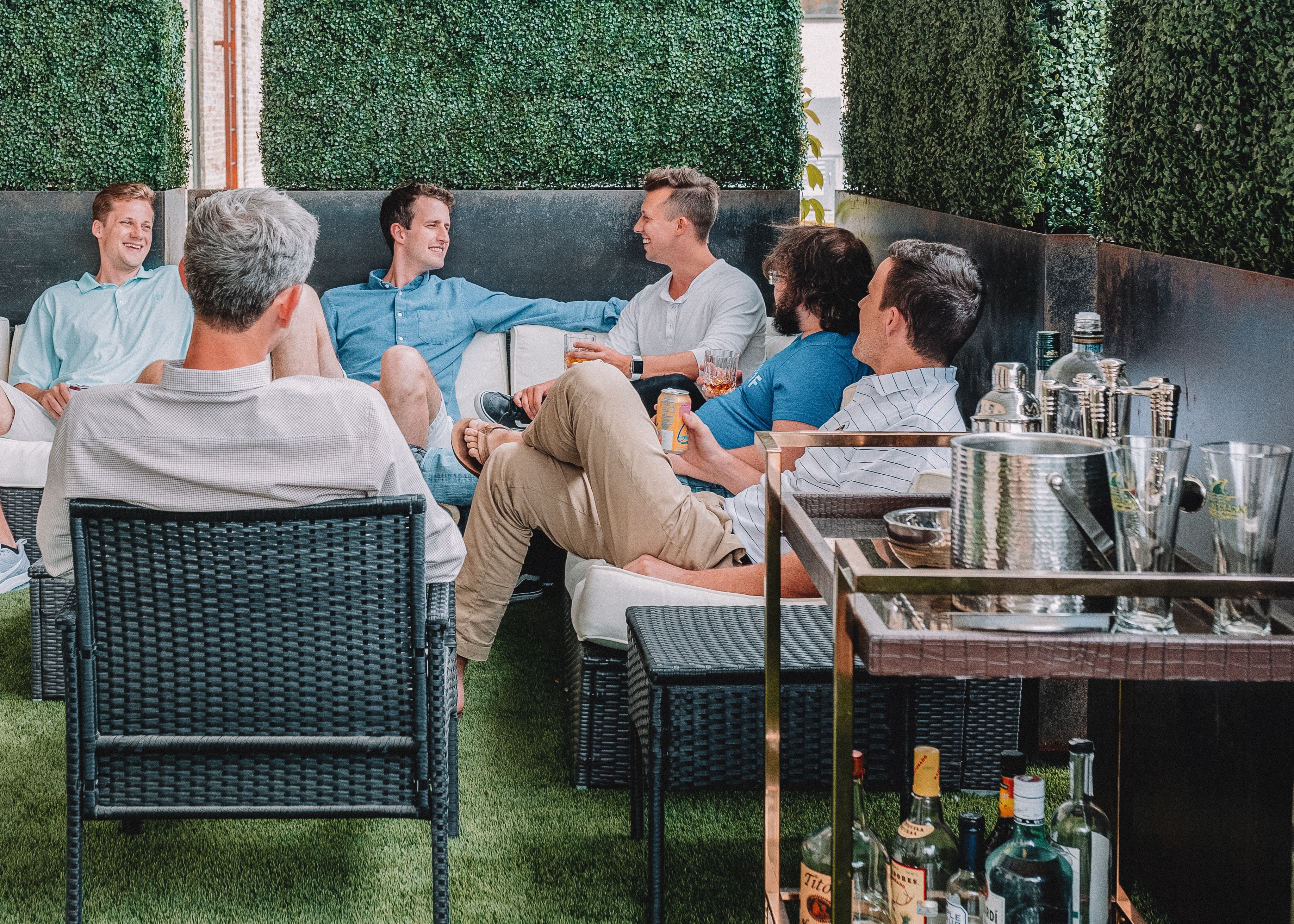 The picture in the section that begins with “industry leaders” shows a group of middle-aged businessmen in casual wear sitting on an L-shaped couch with a hedge screen in a raised grey planter with a solid green well-trimmed hedge. An older, well-groomed man sits in a chair with his back to the camera. The furniture is patio high-end medium grey wicker. They look like they are having a casual conversation